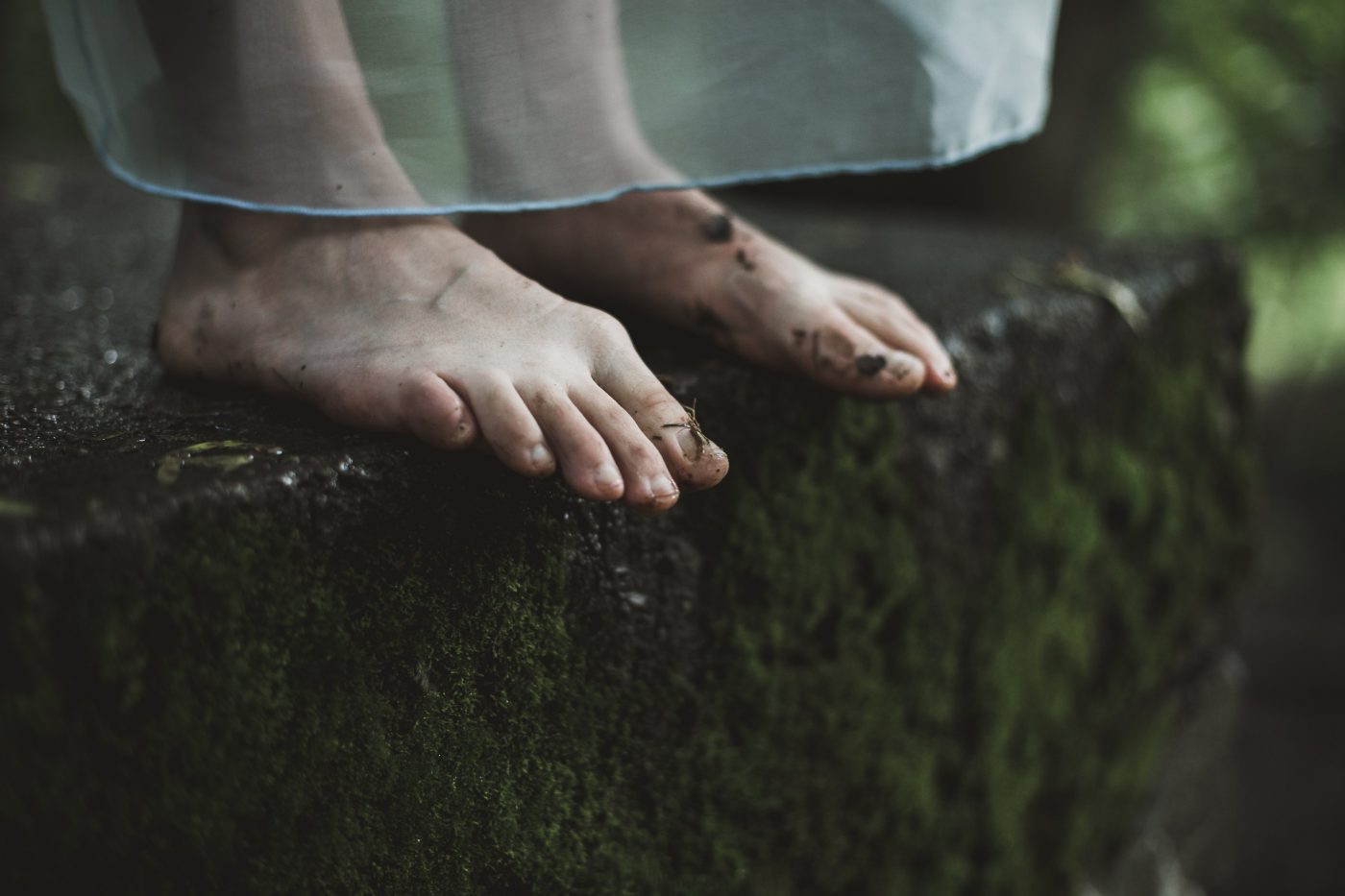 A woman in a sheer white dress standing on moss covered steps