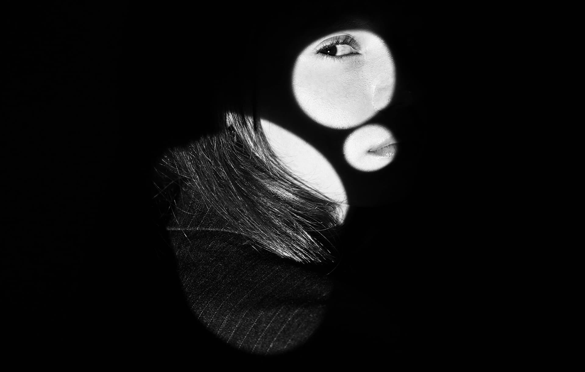 The left side of a woman's face coming out of the shadows.